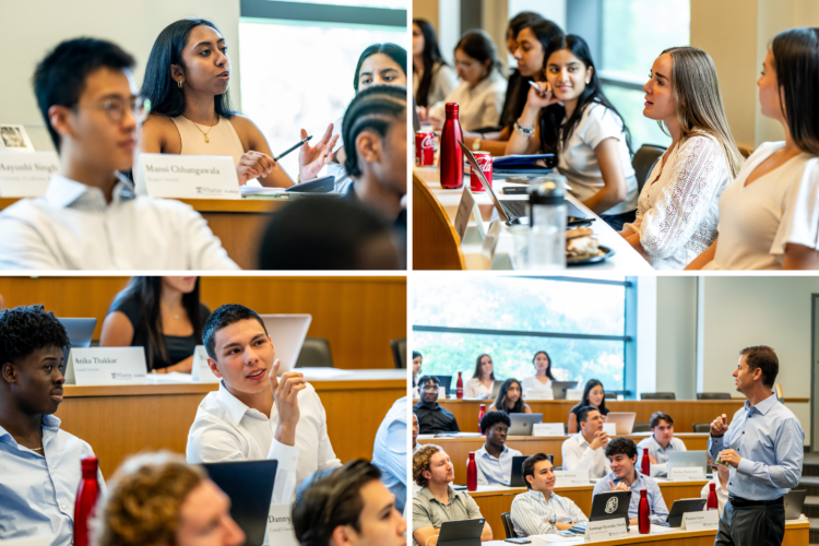 A classroom setting with students and a lecturer engaged in discussion. Students are seated at desks with laptops and notepads, while the lecturer stands, addressing the class.